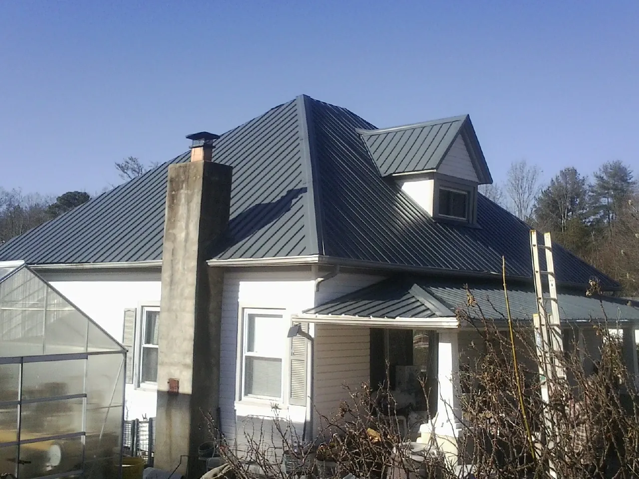 Dark blue standing seam metal roof on a white farmhouse with dormer — Slate & Tile Roof Repair by Roofing Brothers in Muscatine