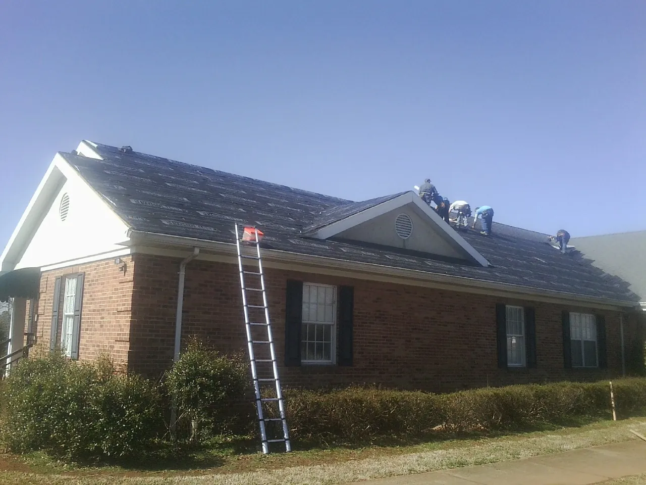 Crew tearing shingles off a brick ranch roof with a ladder set — Metal Roof Repair work by our crew in Muscatine