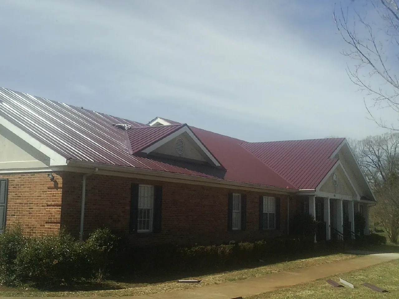 Red metal roof with gabled entries on a long brick building, from a Hail Damage Roof Repair job in Muscatine