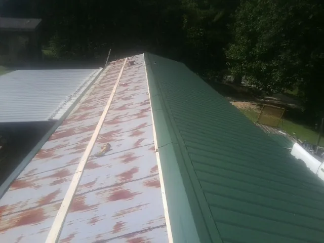 Old rusted panels beside newly installed green metal roofing — Wind Damage Roof Repair by Roofing Brothers in Muscatine