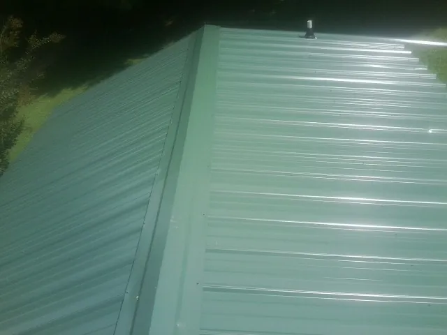 New green metal panels meeting at the ridge of a roof — Flat Roof Repair work by our crew in Muscatine
