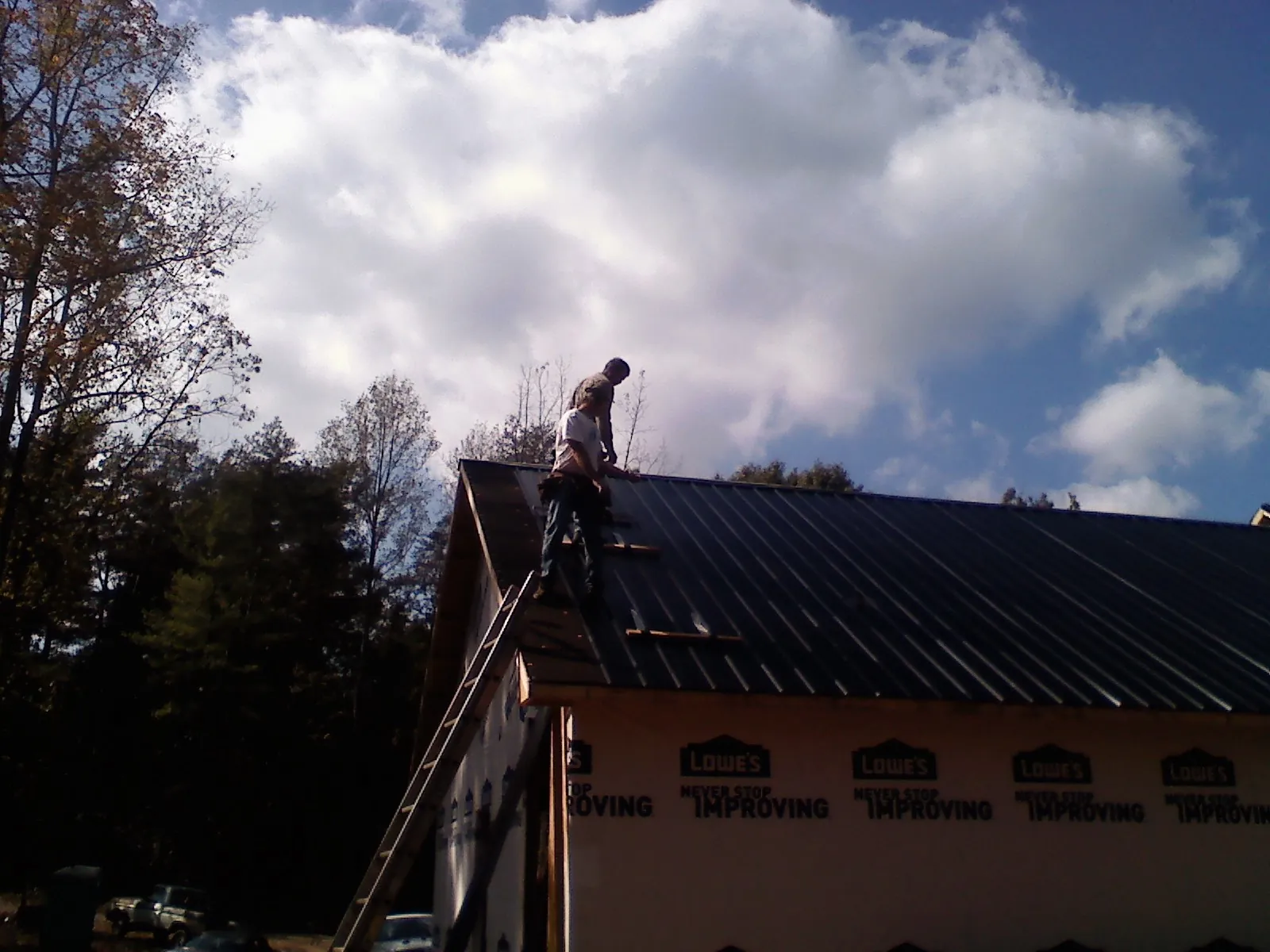 Roofer fastening dark metal panels high against a cloudy sky, from a Roof Inspection job in Muscatine