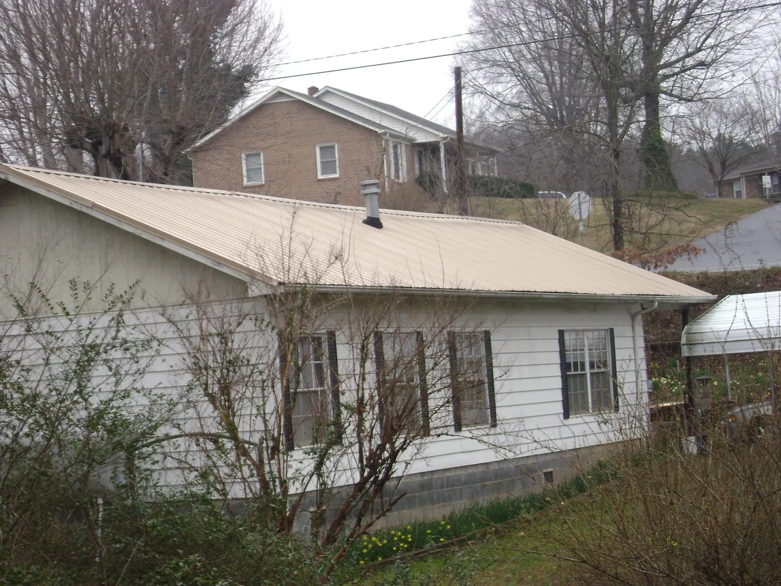 Tan metal roof on a white sided house set into a hillside — Commercial Roofing by Roofing Brothers in Muscatine