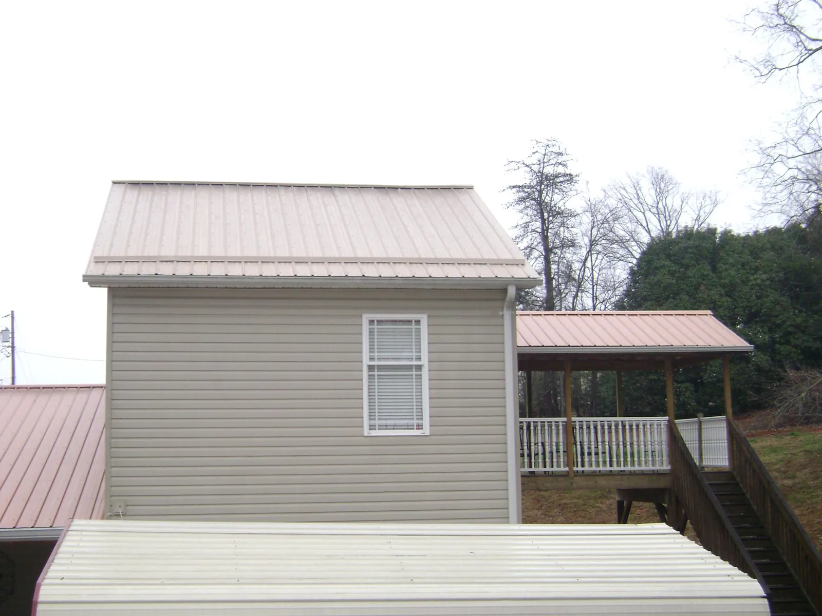 Tan metal roofs on a two story addition and attached porch, from a Roof Replacement job in Muscatine